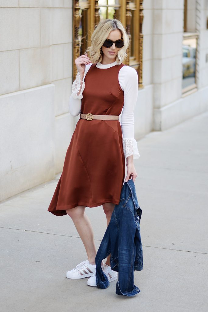 rust colored asymmetrical dress layered over a bell sleeve top with adidas superstars and gucci belt