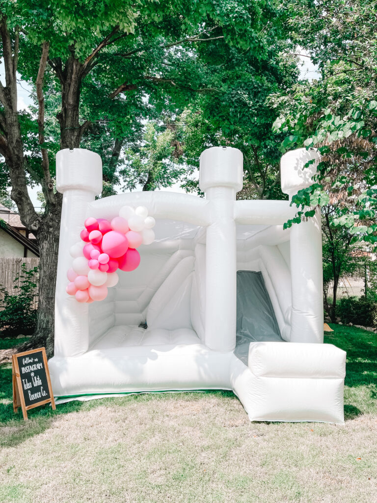 white bounce house with balloon garland for baby girl balloon themed party