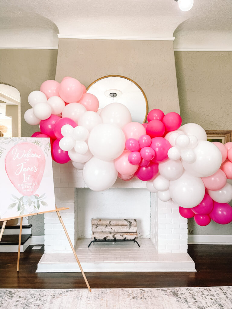 Pink and white balloon arch over fireplace for baby girl balloon themed party