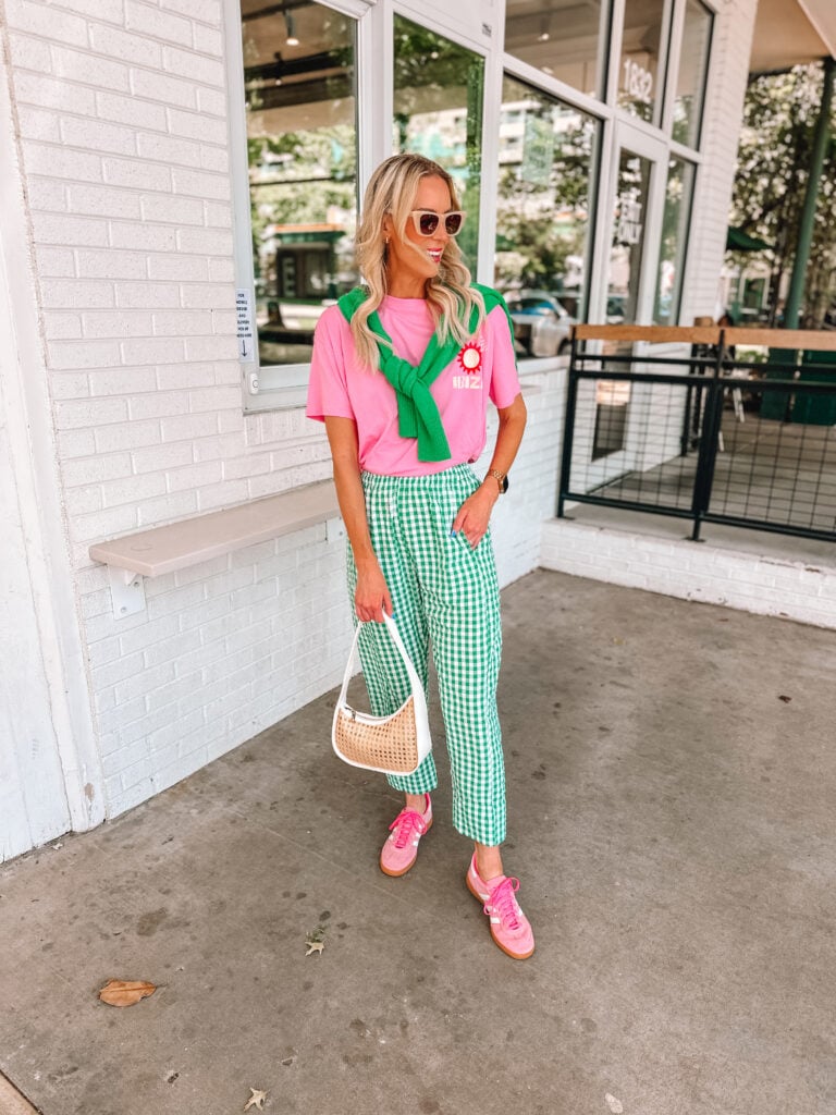 Green plaid pants, pink graphic tee, pink sneakers, and green sweater over shoulders. dopamine dressing outfit idea. 